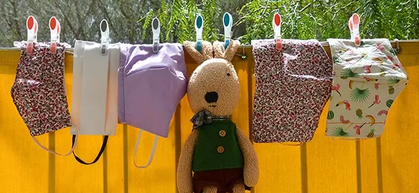A clothesline in the back yard of a home.  A plush rabbit is pegged in the center of the line, with reusable cloth face masks drying on either side.