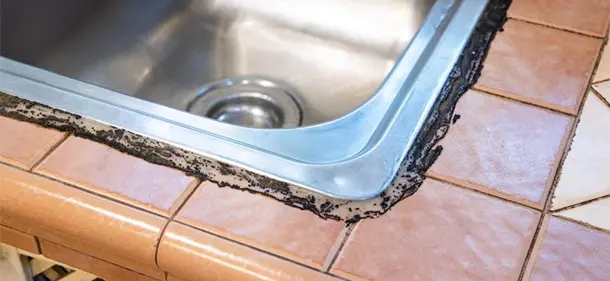 Corner of a kitchen sink with black grime along the outside of the sink