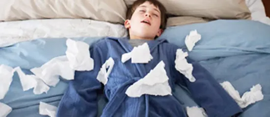 Sick child in robe lying on top of bed covered in used tissues