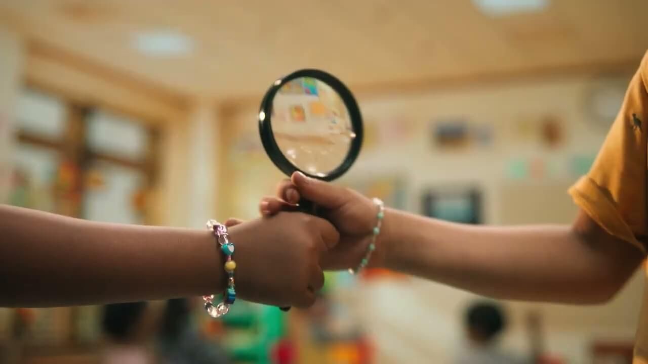 Two children holding a magnifying glass with beaded bracelets on their wrists.