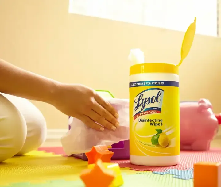 Parent kneeling on floor and wiping baby toys next to canister of Lysol Disinfectant wipes