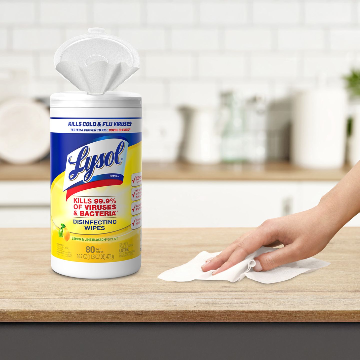 A container of Lysol disinfecting wipes on a kitchen counter with a hand using a wipe.