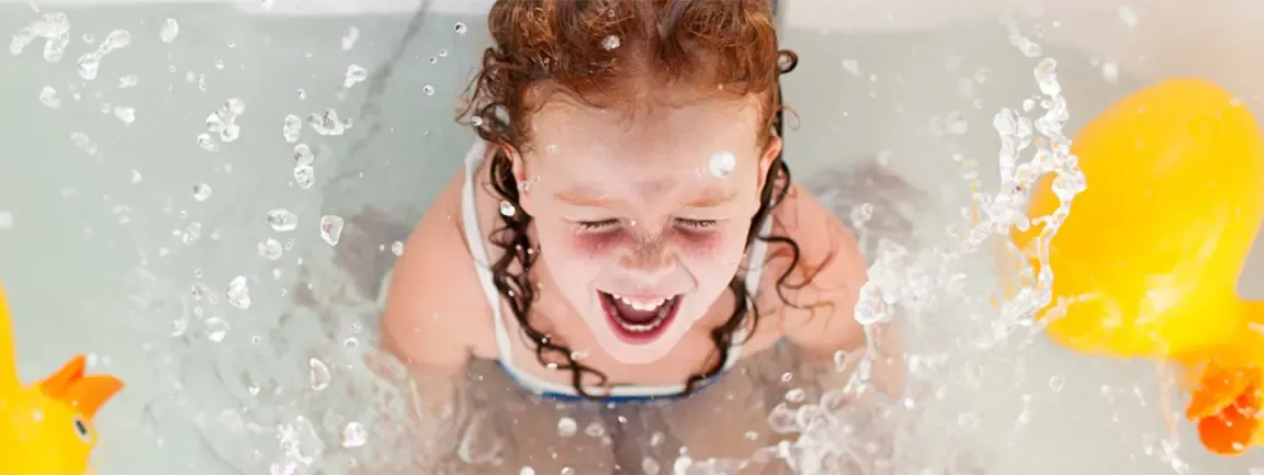 Child laughing in bath surrounded by rubber ducks