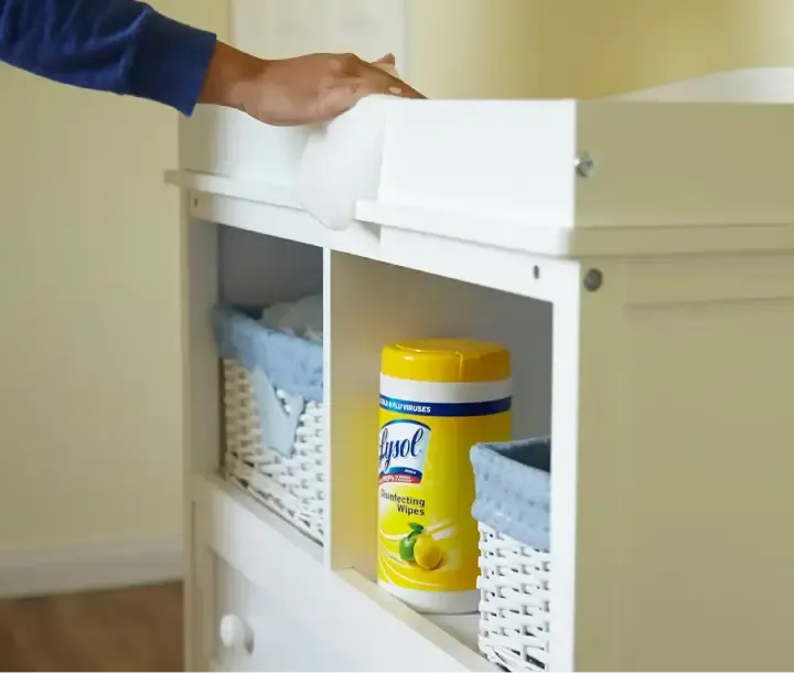 Person wiping cabinet with baskets and canister of Lysol Disinfecting Wipes on shelf