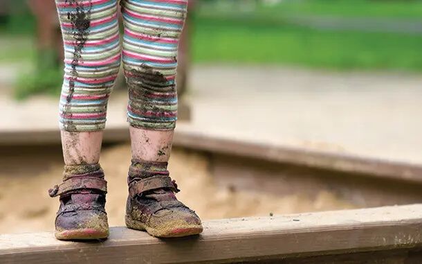 Legs and feet of muddy child in sand pit