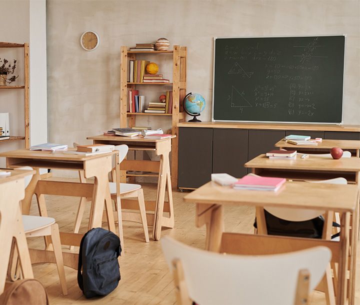 A classroom with wooden desks and chairs, a bookshelf filled with books and a globe, and a chalkboard with mathematical equations.